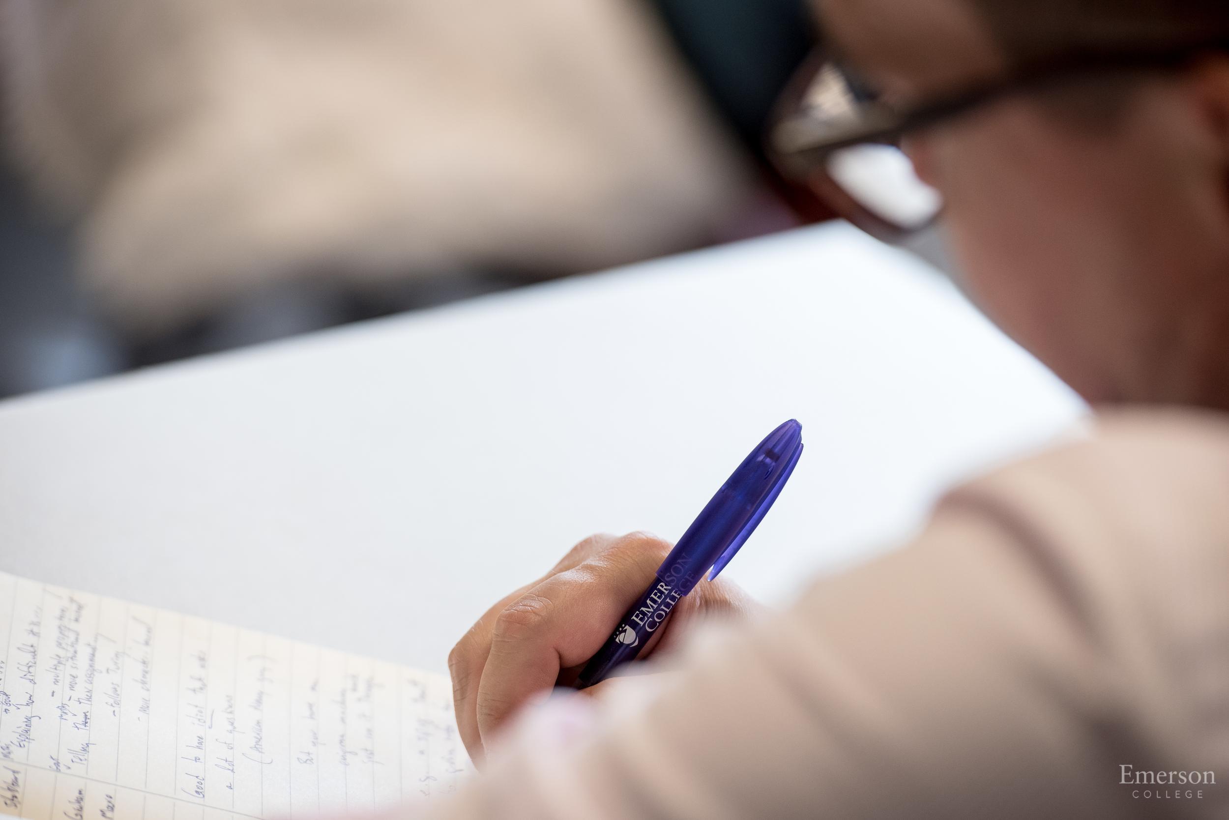 Close-up of a person’s hand writing on paper with a purple Emerson pen